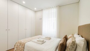 A bedroom with a bed, a nightstand, a wardrobe, and a window with curtains.