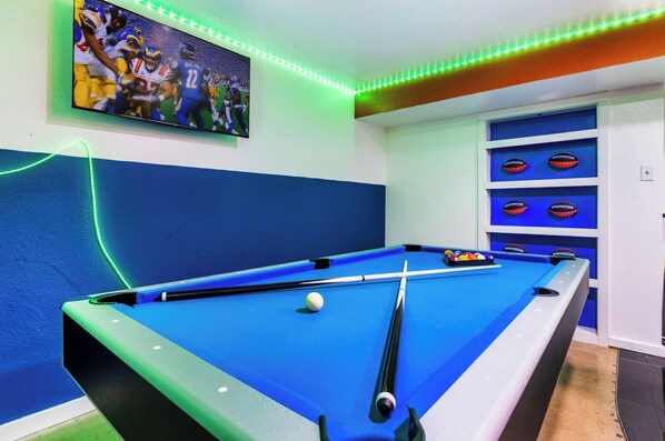 A pool table with a single white ball, surrounded by blue cushions, in a room with blue walls and a ceiling with green LED lights.