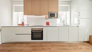 Une cuisine moderne avec des meubles blancs, un four à micro-ondes encastré, un four en acier inoxydable et des panneaux de plafond en bois.