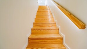 Un escalier en bois, avec des murs blancs et une main courante sur le côté droit.