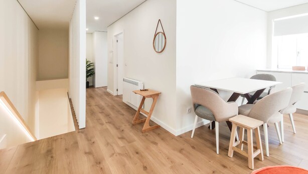 Une cuisine moderne avec un plan de travail blanc, un tabouret en bois et une table à manger avec quatre chaises.