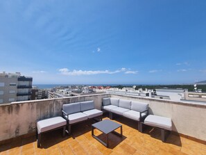 Une terrasse sur le toit, aménagée avec un ensemble de canapés et une table basse, offrant une vue sur le paysage urbain et la mer.