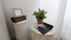 A framed picture on a shelf, a potted plant on a round wooden table, and a black notebook with a pen on it.