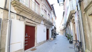 A narrow cobblestone street flanked by historic buildings with balconies, a bicycle parked on the right, and a red door on the left.