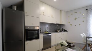 A modern kitchen with stainless steel appliances, white cabinetry, and a clock on the wall.