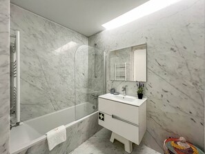 Une salle de bain moderne avec un mur en marbre, une douche en verre, un meuble-lavabo blanc avec un miroir et une petite plante en pot.