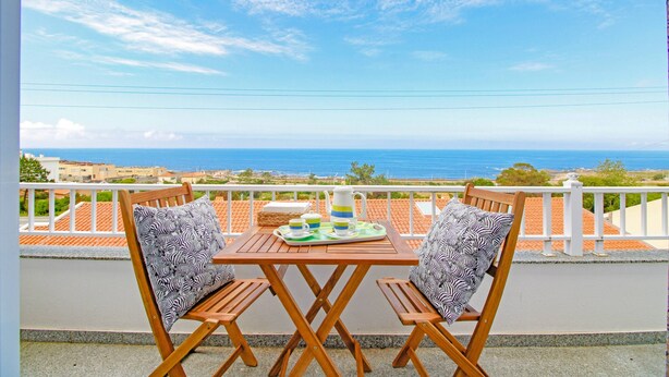 Un balcón con una mesa lista para dos personas, con vistas a la costa.