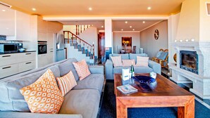 Una sala de estar moderna con sofá, mesa de centro y chimenea. Se ve una escalera que conduce a otro nivel.