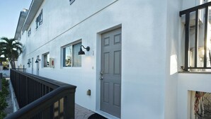 A white building with a grey door, a black railing, and a small black mat at the entrance.