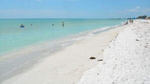 A beach with clear turquoise water, a sandy shore, and a few people in the distance.