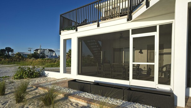 A modern building with a balcony, large windows, and a sandy ground area.