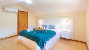 A bedroom with a bed, bedside table, nightstand, and an air conditioning unit.
