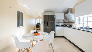 A modern kitchen with white cabinets, a stainless steel refrigerator, and a dining area with white chairs and a table set for two.