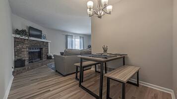 A modern living room with a fireplace, a sofa, a dining table with benches, and a chandelier.