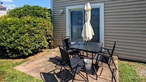An outdoor patio with a table and chairs, a window with an umbrella, and a hedge. - Cozy & Charming 2-bedroom, 2 bath in Central location near Cincinnati (Erlanger)