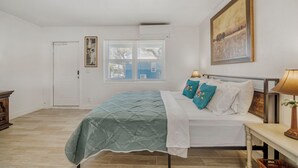 Une chambre à coucher avec un lit, une table de chevet, une lampe, un tableau et une fenêtre avec des stores.