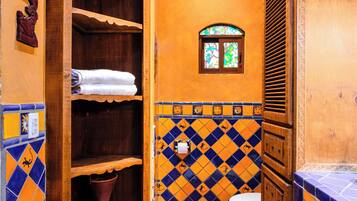 A bathroom with a wooden cabinet, a tiled floor with a geometric pattern, a white toilet, and a small window with stained glass.