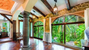 A spacious room with a polished wooden floor, large arched windows, stone walls, and a high ceiling with exposed beams. - La Hacienda Hotel, at Xcaret (Playa del Carmen)