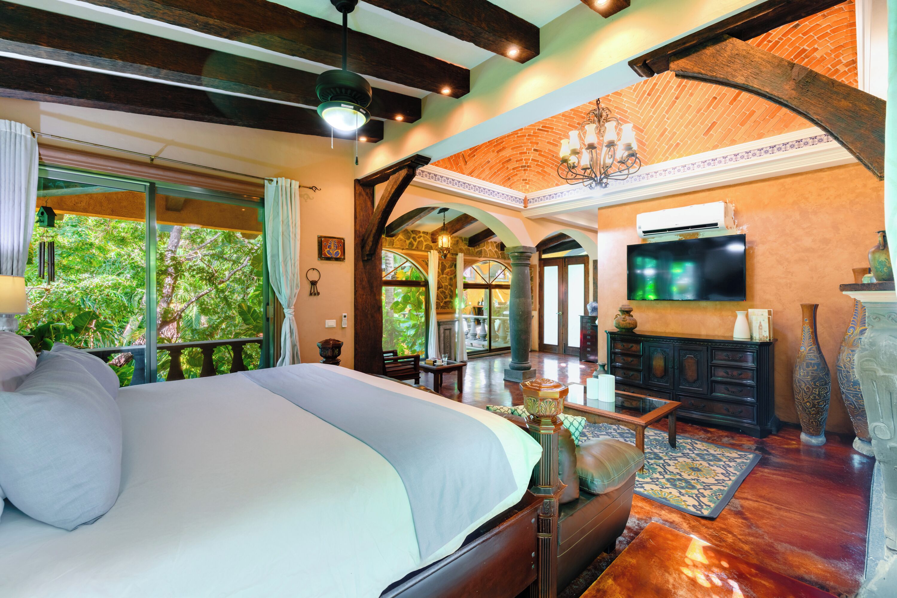 Un dormitorio amplio con una cama grande, televisor y vistas a la exuberante vegetación.