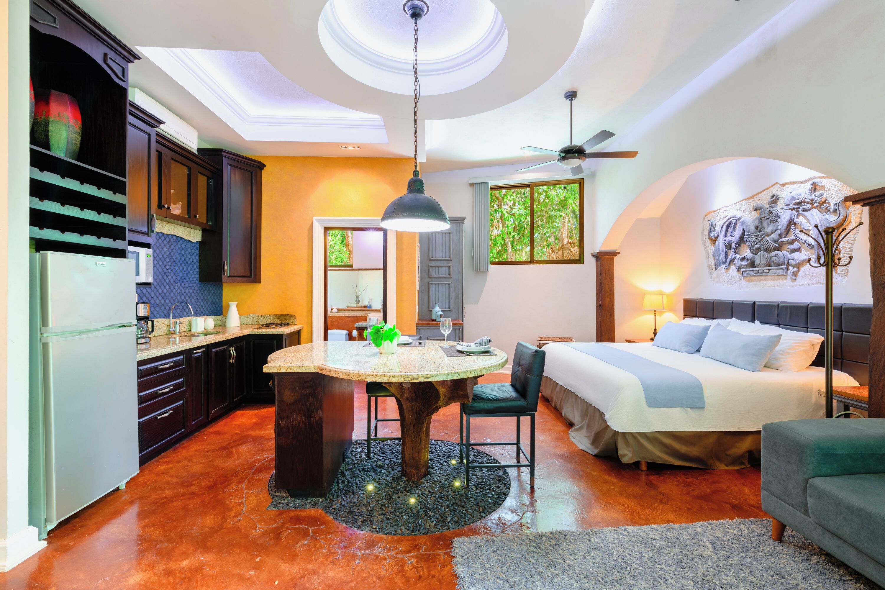 Una cocina moderna con comedor, un dormitorio con cama grande y ventilador de techo, y un baño con ducha e inodoro.