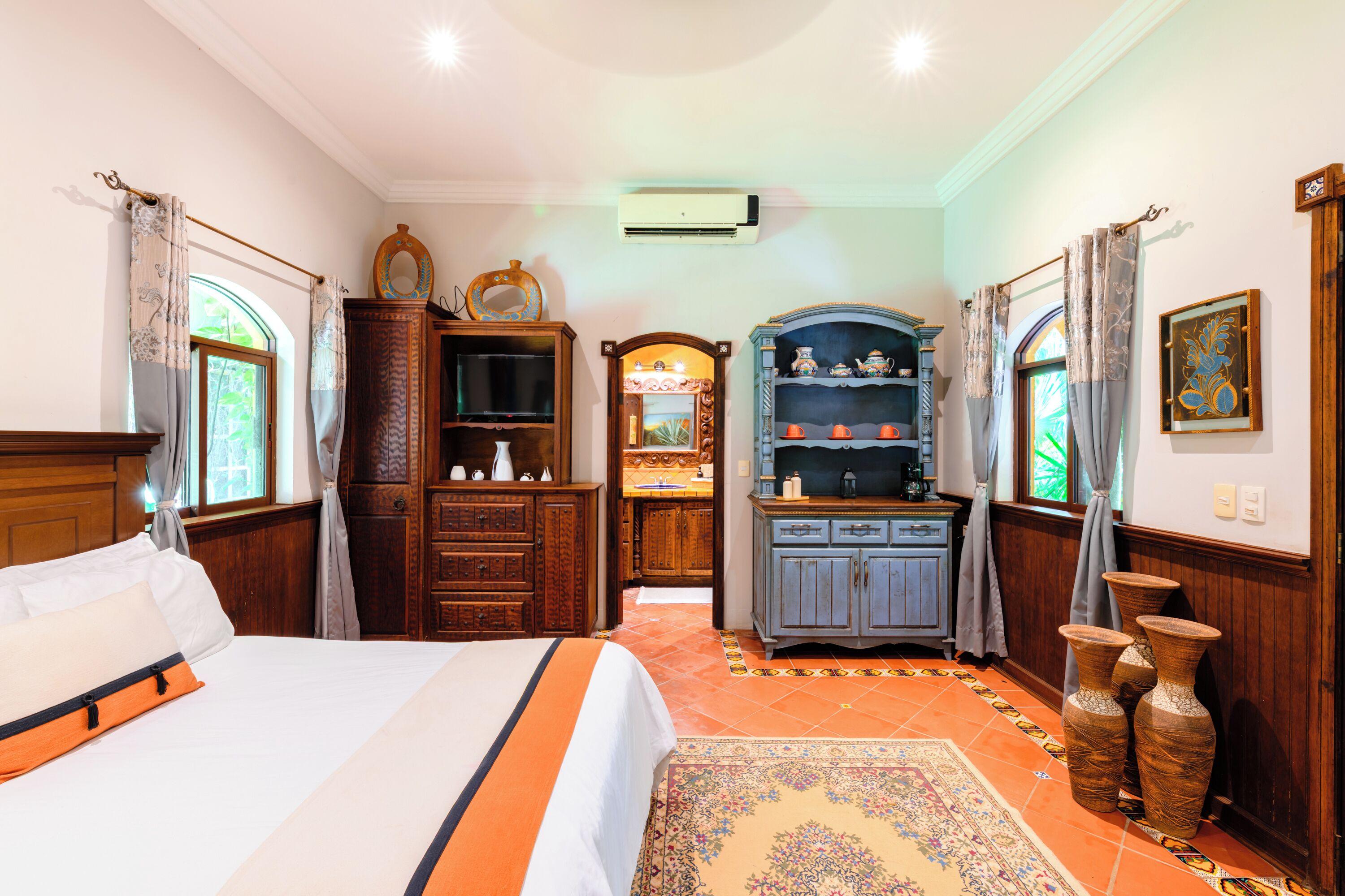 A bedroom with a bed, wooden dresser, and a vanity with a mirror.