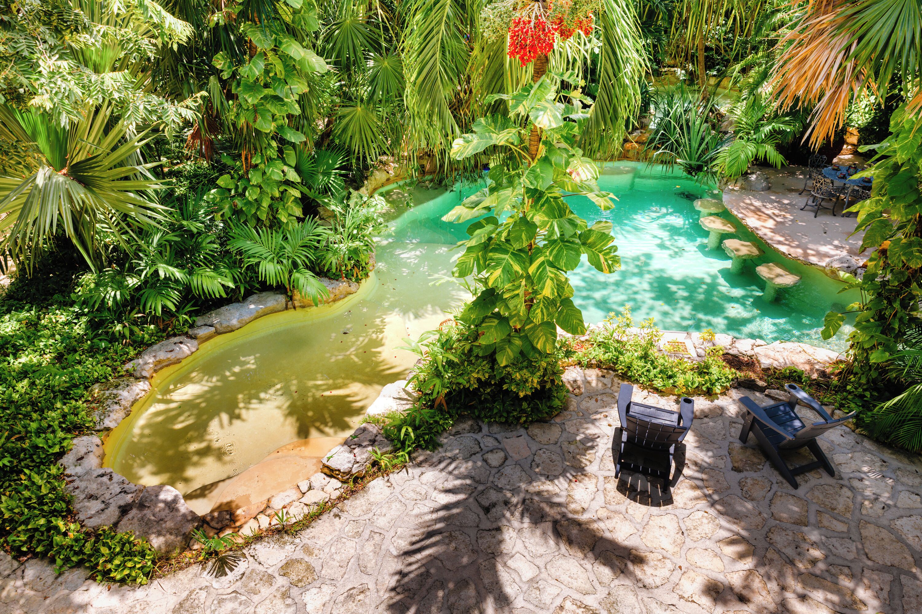 Ein Garten mit einem kleinen Teich, einem gepflasterten Weg und zwei Holzstühlen.