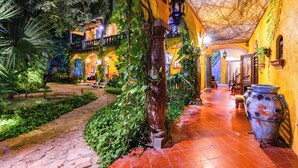 A courtyard with a tiled pathway, lush greenery, and a large decorative pot. - La Hacienda Hotel, at Xcaret (Playa del Carmen)