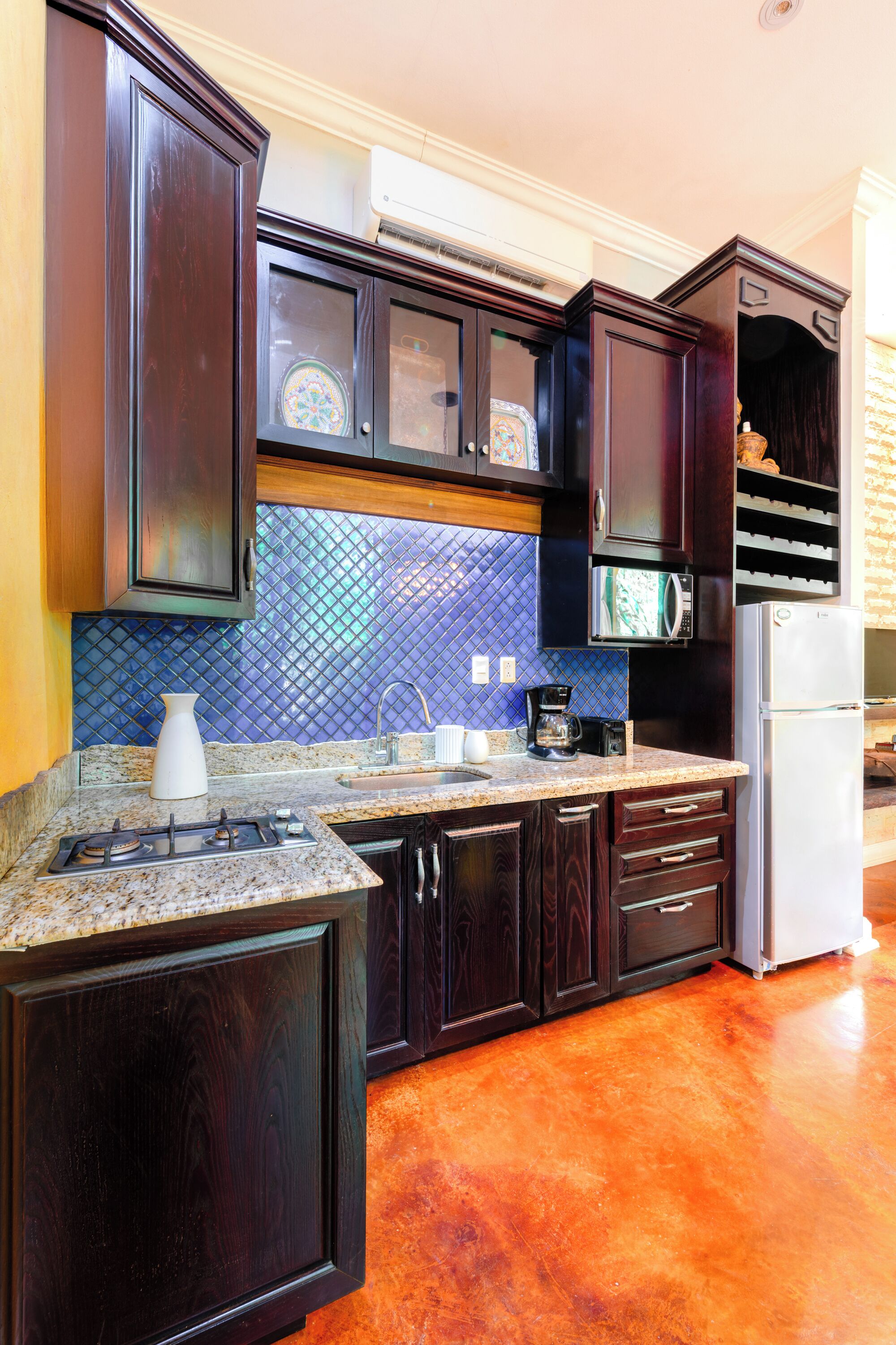 Una cocina con armarios de madera oscura, encimera de granito, refrigerador de acero inoxidable y salpicadero de azulejos azules.