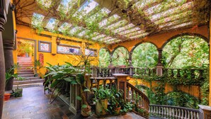 A covered outdoor area with a stone floor, potted plants, and a wooden staircase leading to an upper level. - La Hacienda Hotel, at Xcaret (Playa del Carmen)
