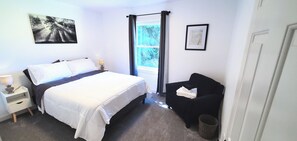 A bedroom with a bed, bedside table, lamp, window with curtains, and a black chair. - Newly remodeled home on 2 acres. Close to Mt Baker Ski Area,Bellingham & Canada! (Bellingham)