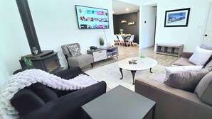 Un salon moderne avec une cheminée, des sièges confortables, un téléviseur à écran plat et un coin repas à l’arrière-plan.