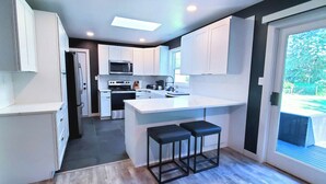 Une cuisine moderne avec des meubles blancs, un îlot central doté de tabourets, un four à micro-ondes, une cuisinière et un réfrigérateur.