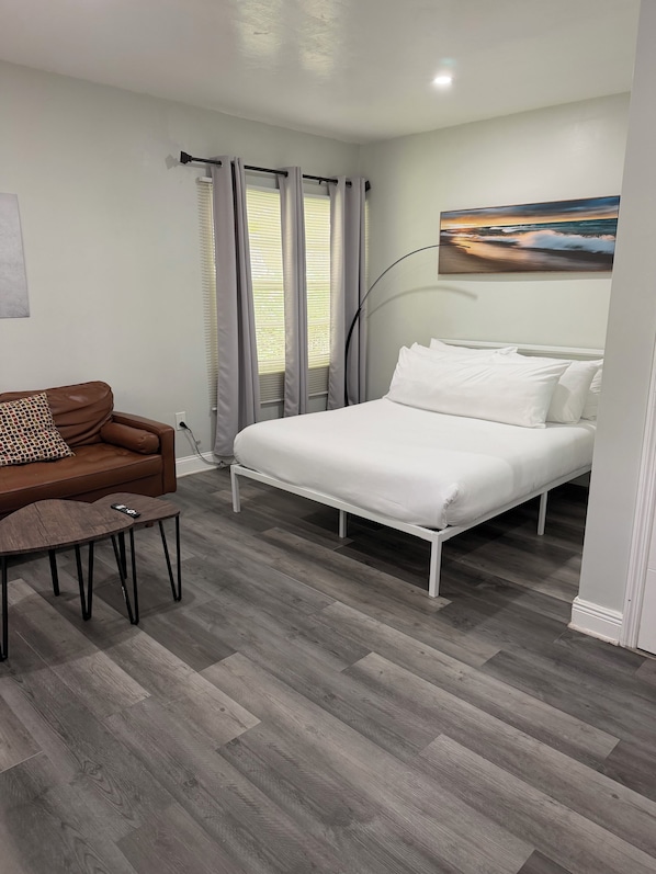A bedroom with a bed, a brown sofa, a small table, and a painting on the wall.