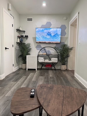A modern living room with a mounted TV, a round coffee table, a hanging chair, and a built-in heater.