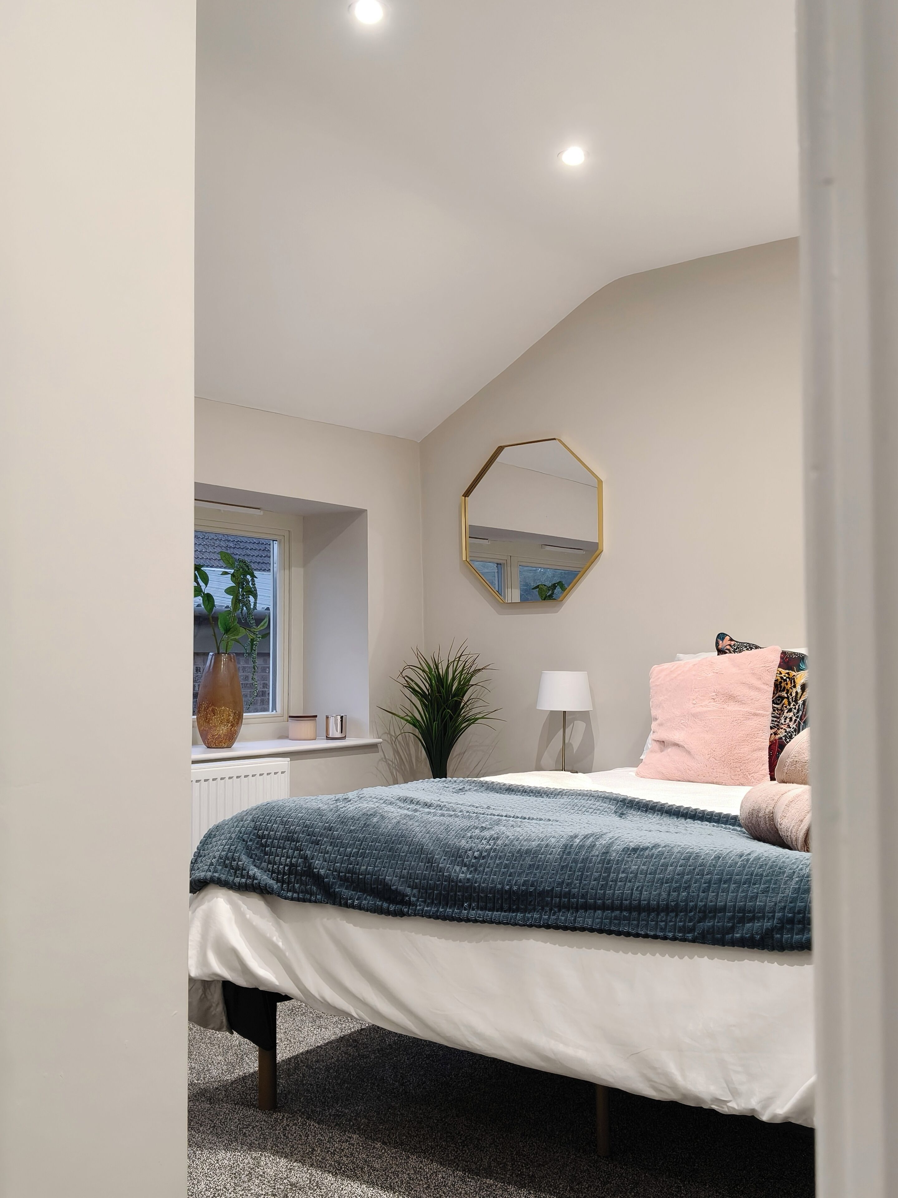 A bedroom with a bed, a window, a mirror, and a plant.