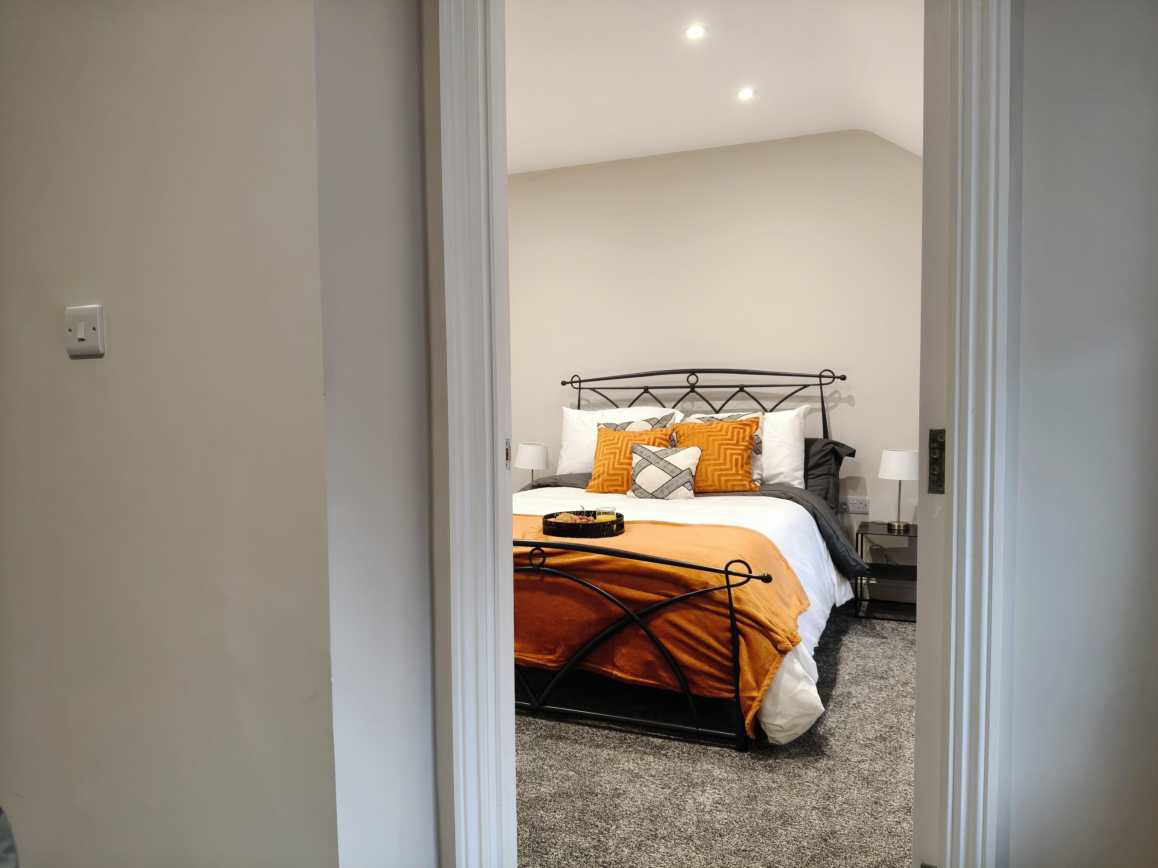 Een slaapkamer met een bed, kussens, een nachtkastje en een lamp.
