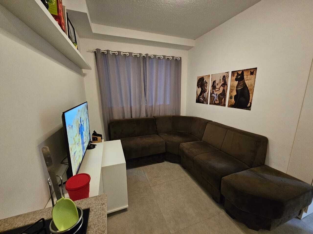A living room with a brown sectional sofa, a flat-screen TV, a small white table, and a red trash bin.