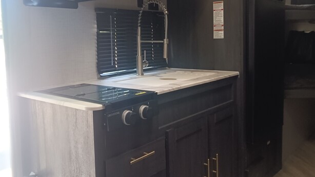 Una cocina con microondas, estufa y horno integrados. Hay un lavamanos de acero inoxidable y un extintor colgado en la pared.