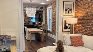 A cozy living room with a dog on a white sofa, a patterned rug, and a brick wall. - Charming and walkable downtown Denver RINO 3 bed home (Denver)