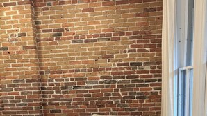 A corner room with a brick wall, a beige sectional sofa, and a window with white curtains. - Charming and walkable downtown Denver RINO 3 bed home (Denver)