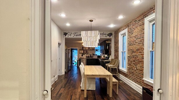 A spacious kitchen with a brick wall, wooden flooring, and a dining area with a table and chairs. - Charming and walkable downtown Denver RINO 3 bed home (Denver)