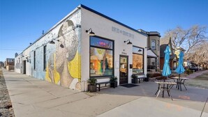 A building with a mural on the side, a sign reading "Rivers and Roads Coffee," outdoor seating with blue umbrellas, and a clear sky. - Charming and walkable downtown Denver RINO 3 bed home (Denver)