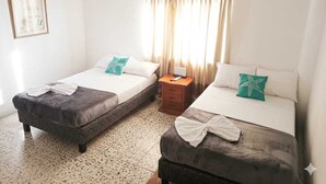 A hotel room with two beds, a nightstand, a framed picture on the wall, and a window with curtains. - Hotel Monte Carlo (Tolú)