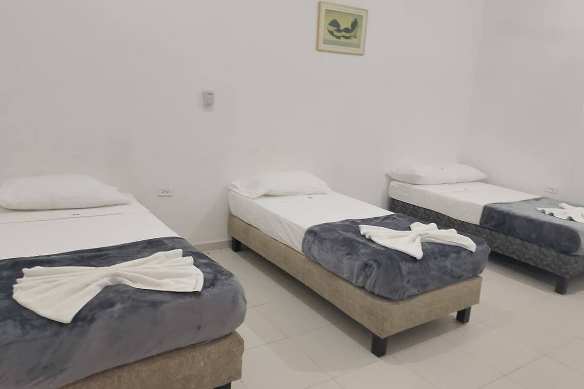 Quarto com três camas de solteiro, cada uma com travesseiro e cobertor.