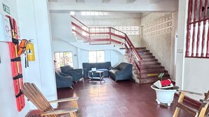 A spacious lobby with a red-tiled floor, a staircase with red balusters, and a seating area with sofas and chairs. - Hotel Monte Carlo (Tolú)
