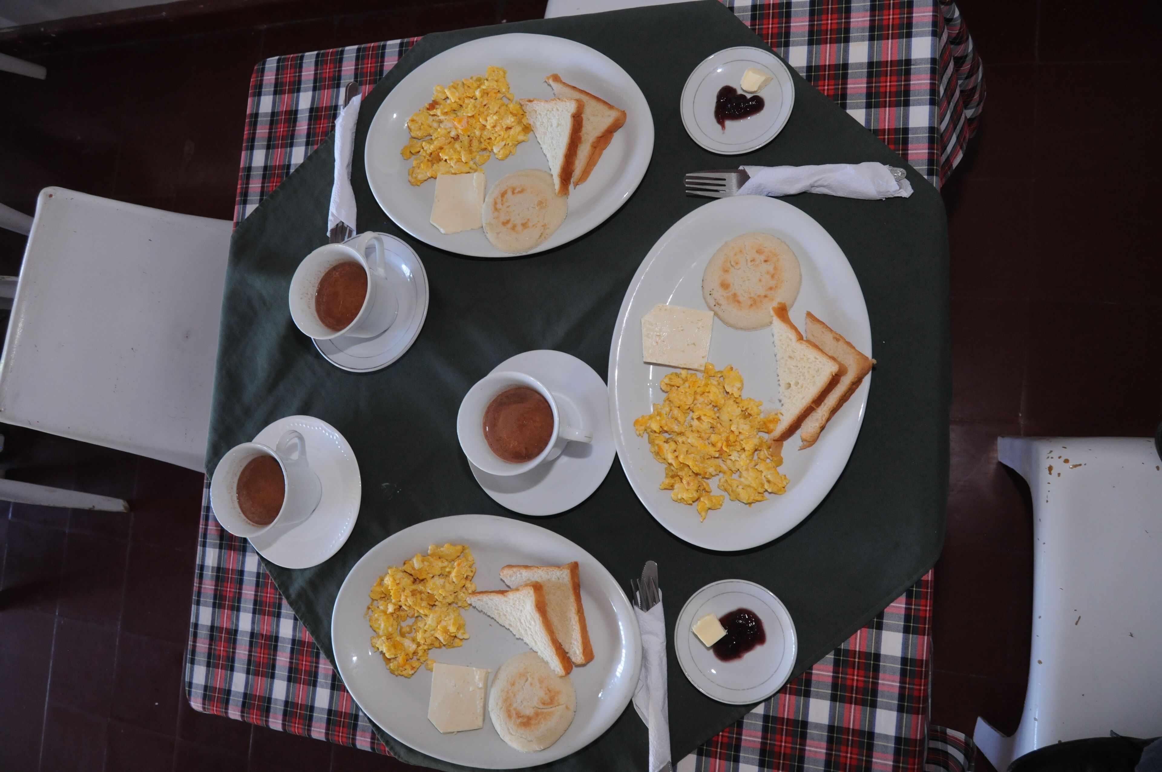 A table set with breakfast plates containing scrambled eggs, toast, and butter, along with cups of coffee and jam.