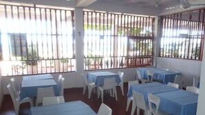 A room with tables and chairs, barred windows, and a ceiling fan. - Hotel Monte Carlo (Tolú)