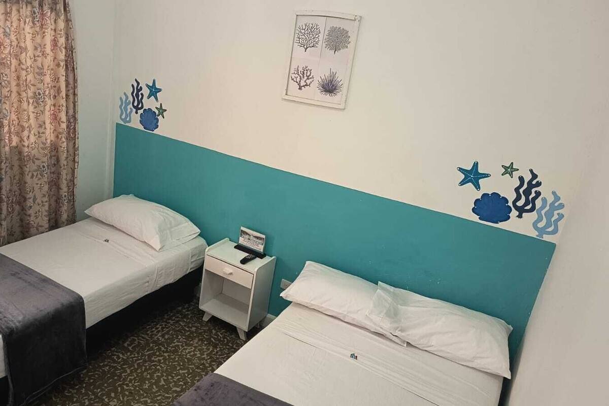 Quarto com duas camas de solteiro, mesa de cabeceira com abajur e janela com cortinas.