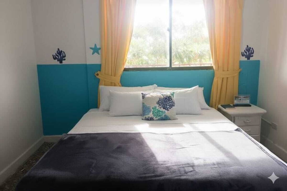 Quarto com cama, mesa de cabeceira e janela com cortinas.