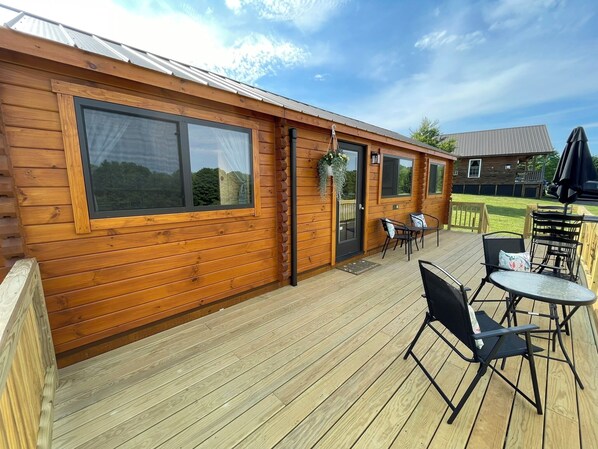 A wooden cabin with large windows, a deck with outdoor furniture, and a visible adjacent building.
